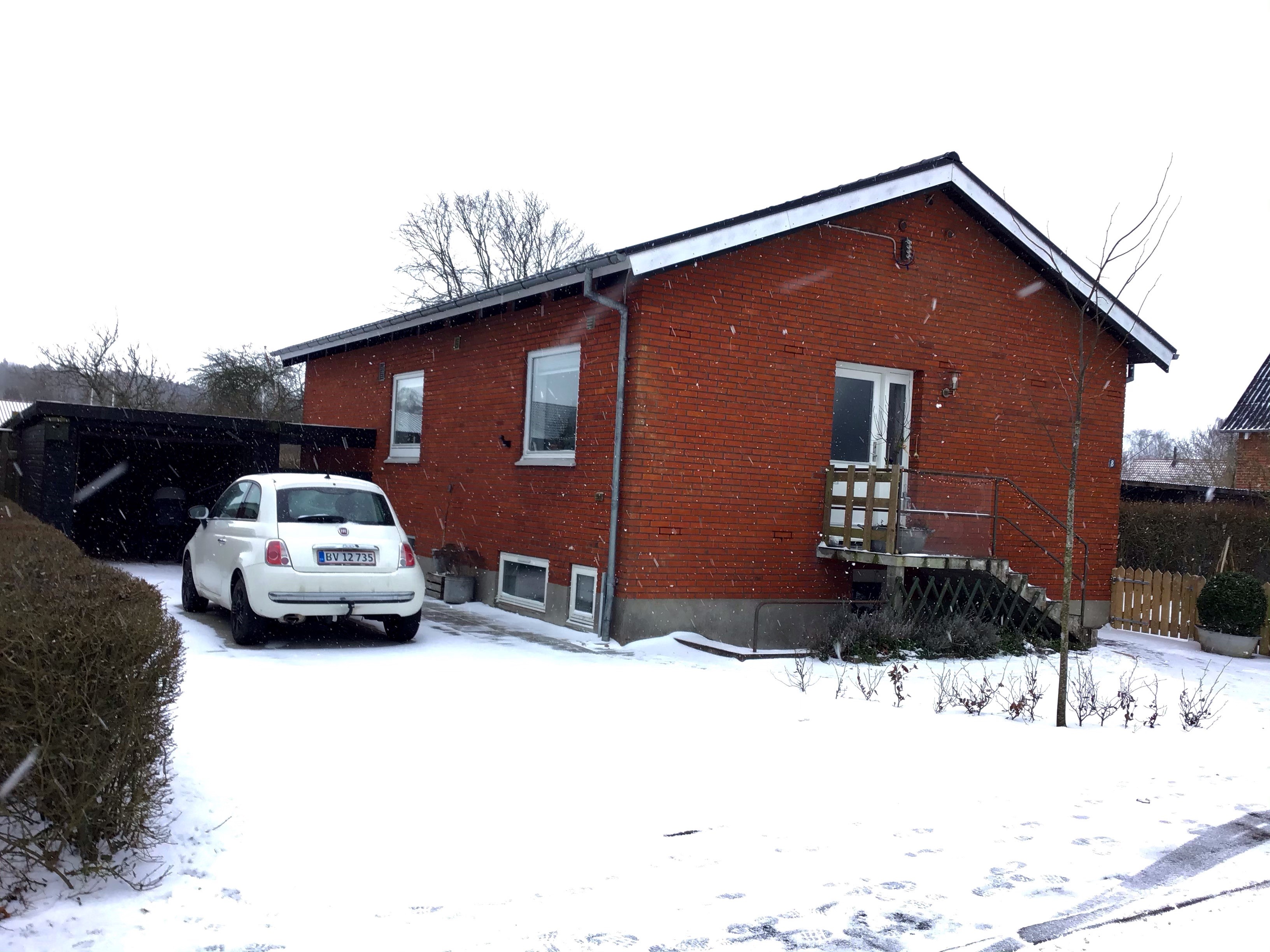 Mariannes hus i røde mursten. Der er holder en bil foran og der er dækket med sne 